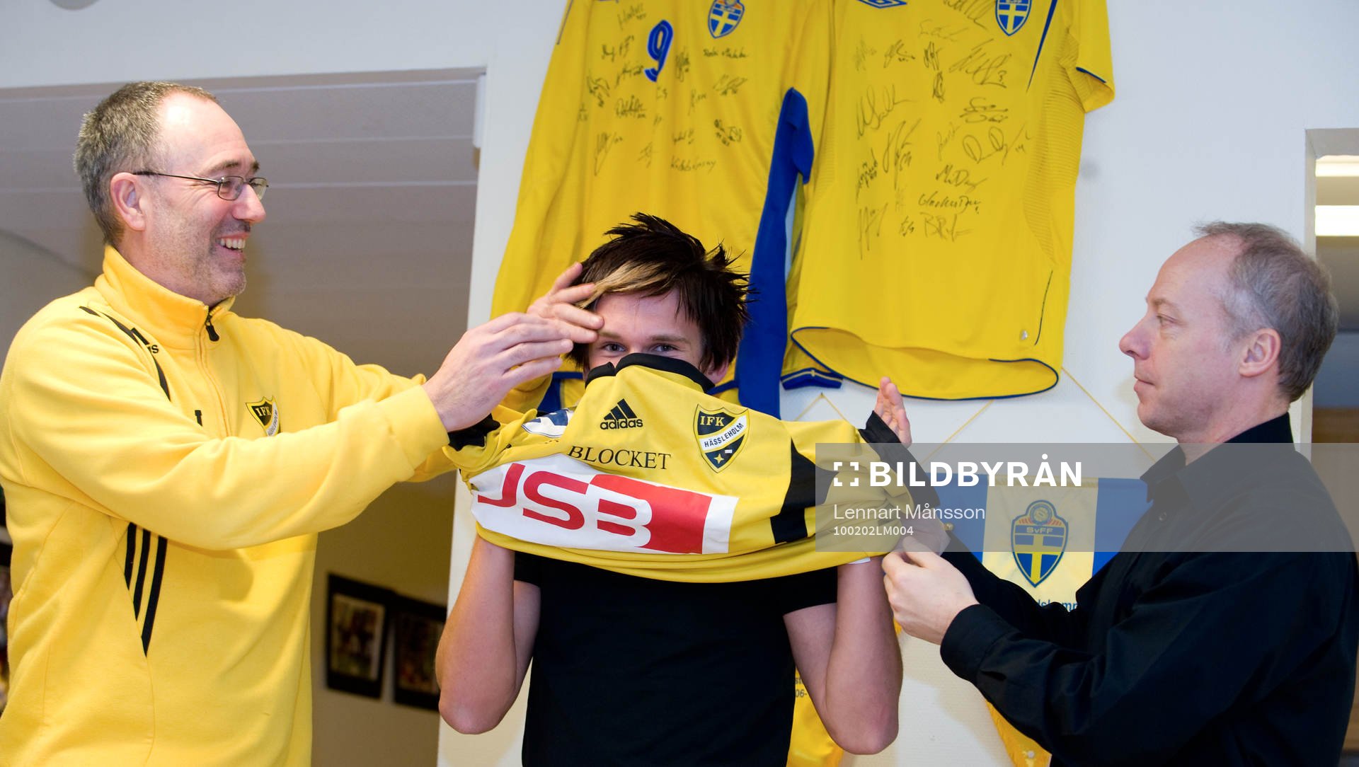  André Bengtsson, 16 år, IFK Hässleholm: Affe Jönsson, tränare, och Michael Engel, värvningsansvarig, hjälper André att ta på IFK-tröjan.
