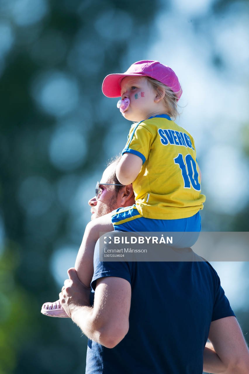 Liten svensk supporter på pappas axlar och med napp i mun
