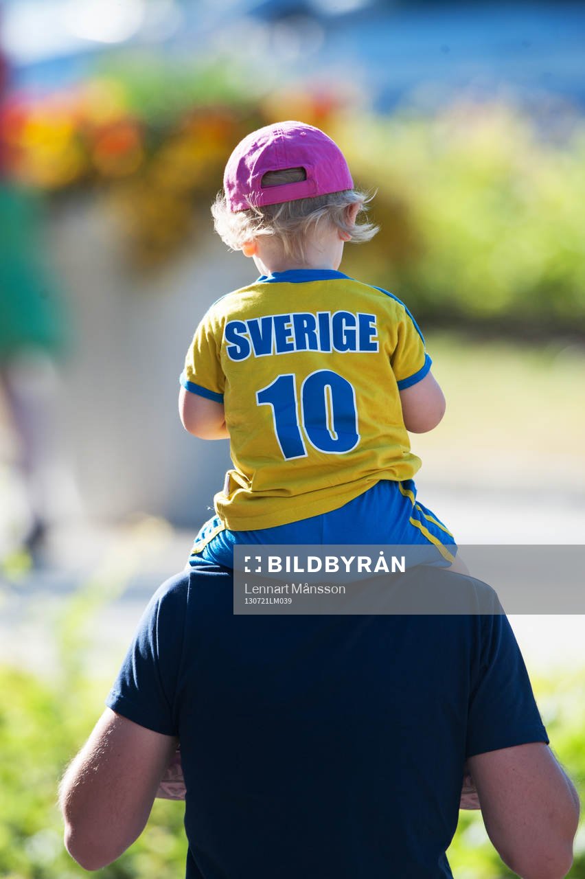 Liten svensk supporter på pappas axlar och med napp i mun