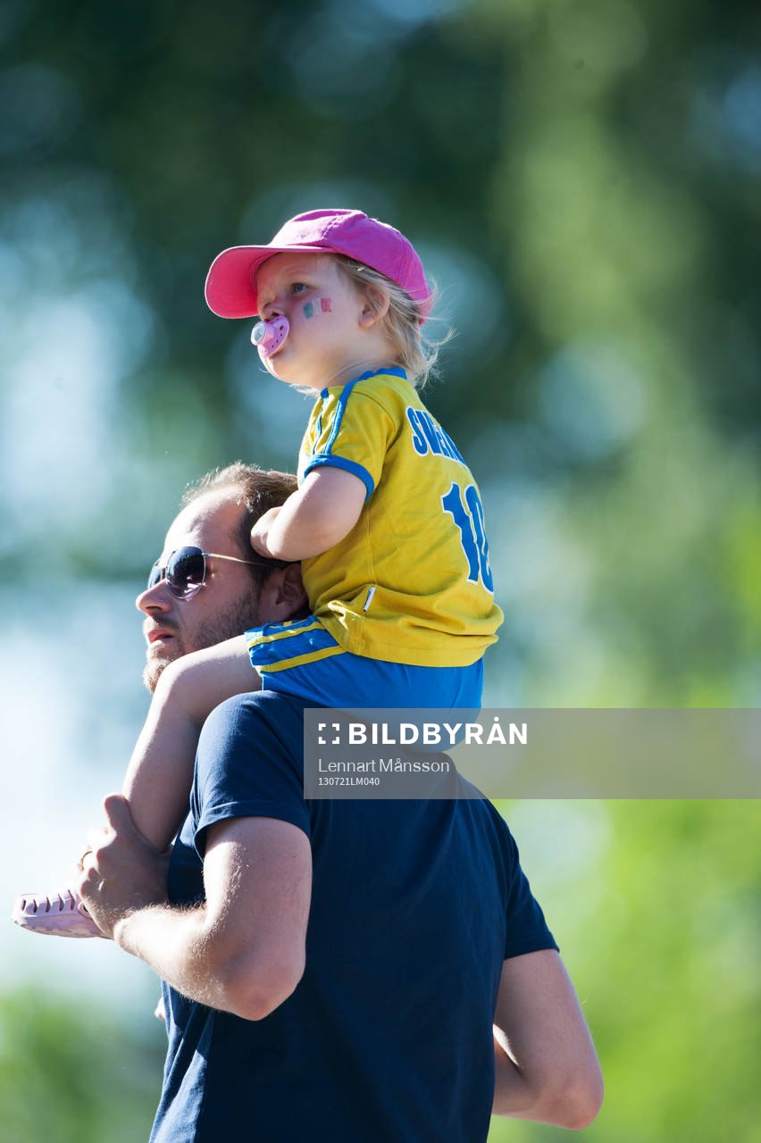 Liten svensk supporter på pappas axlar och med napp i mun