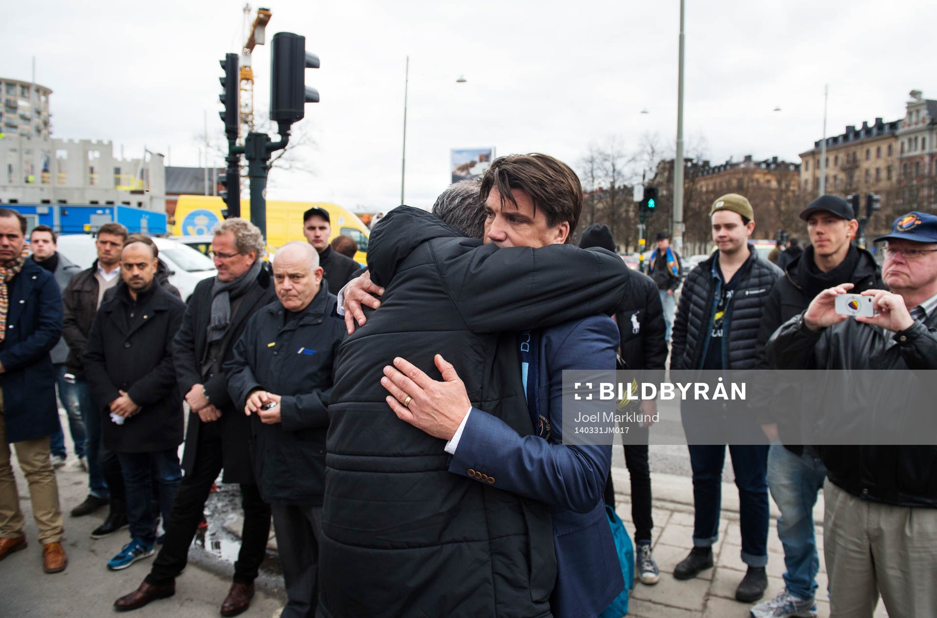 AIK:s ordförande Johan Segui kramar om Djurgårdens sportchef Bosse Andersson i samband med att de hedrar den avlidne djurgårdssupportern Stefan Isaksson med en tyst minut utanför Stadion den 31 mars 2014 i Stockholm. I bakgrunden står svenska fotbollandslagets förbundskapten Erik Hamrén och Svenska Fotbollförbundets generalsekreterare Mikael Santoft.