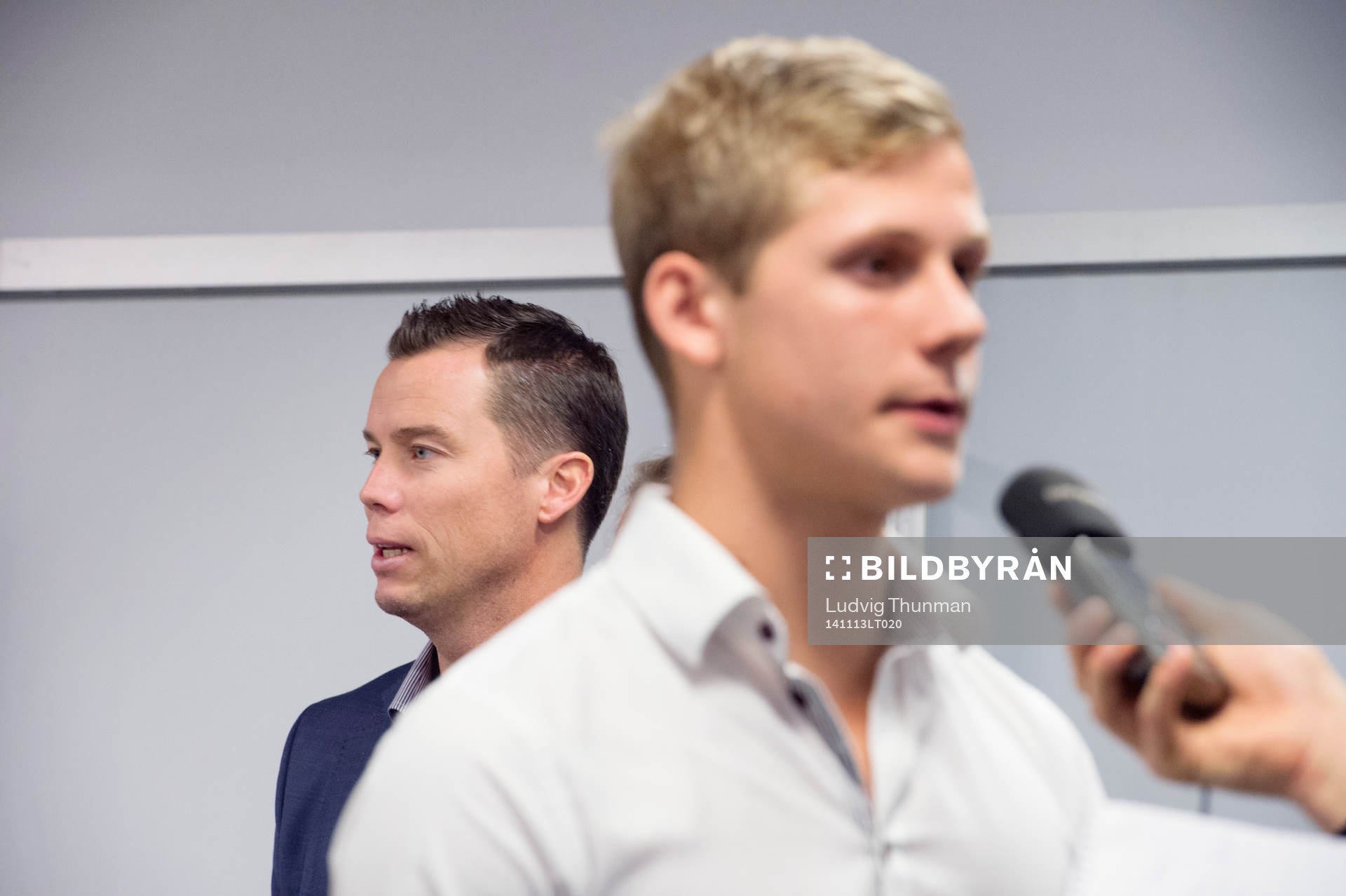 Sportchef Daniel Andersson tittar fram bakom Erik Andersson som intervjuas efter en presskonferens där Malmö FF presenterar nya spelare den 13 november 2014 i Malmö.