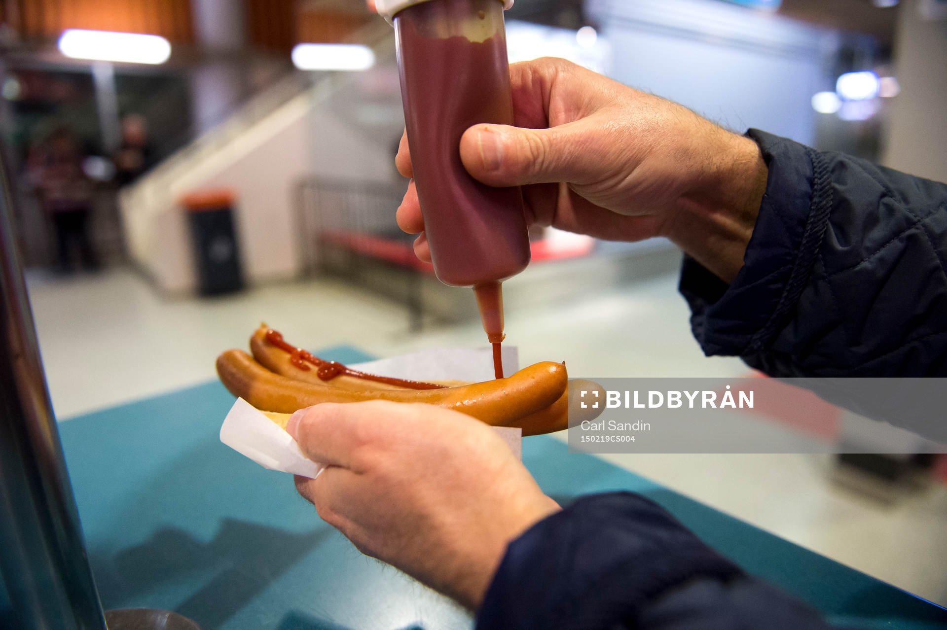 En person tar ketchup på korv med bröd innan en