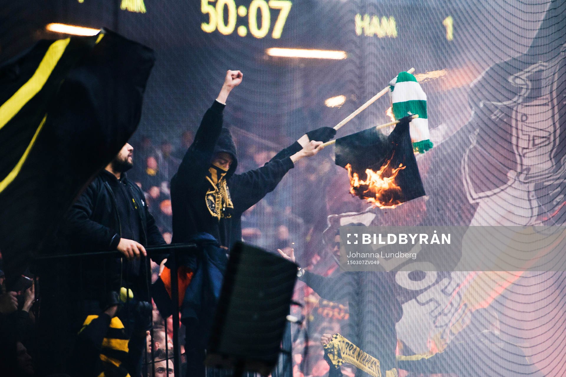 Några AIK supportrar bränner en Hammarby flagga
