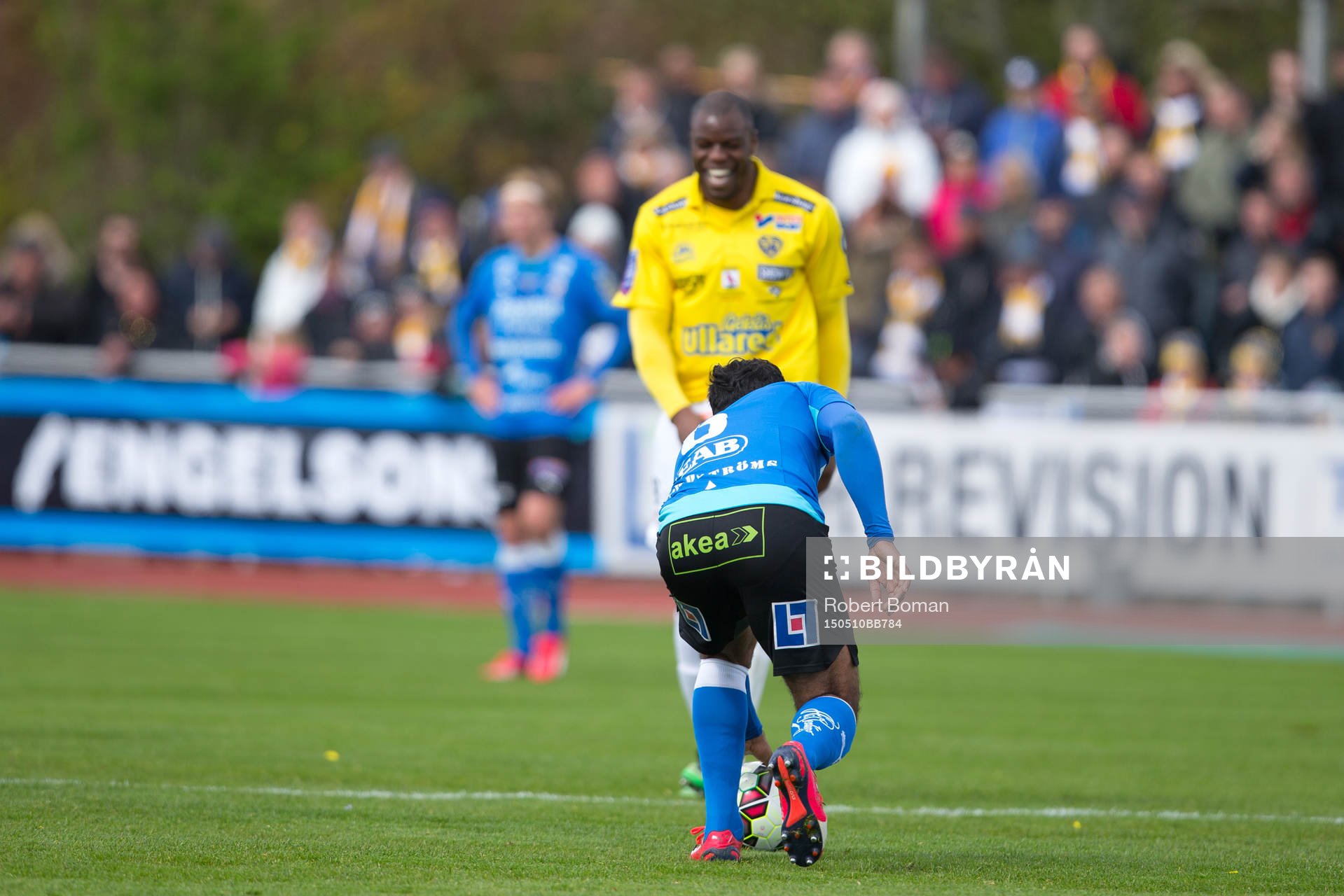 En Halmstads spelare lägger upp bollen för friskark medan Falkenbergs Hakeem Araba skrattar åt domslutet i bakgrunden under fotbollsmatchen i Allsvenskan mellan Falkenbergs FF och Halmstads BK den 10 maj 2015 i Falkenberg.