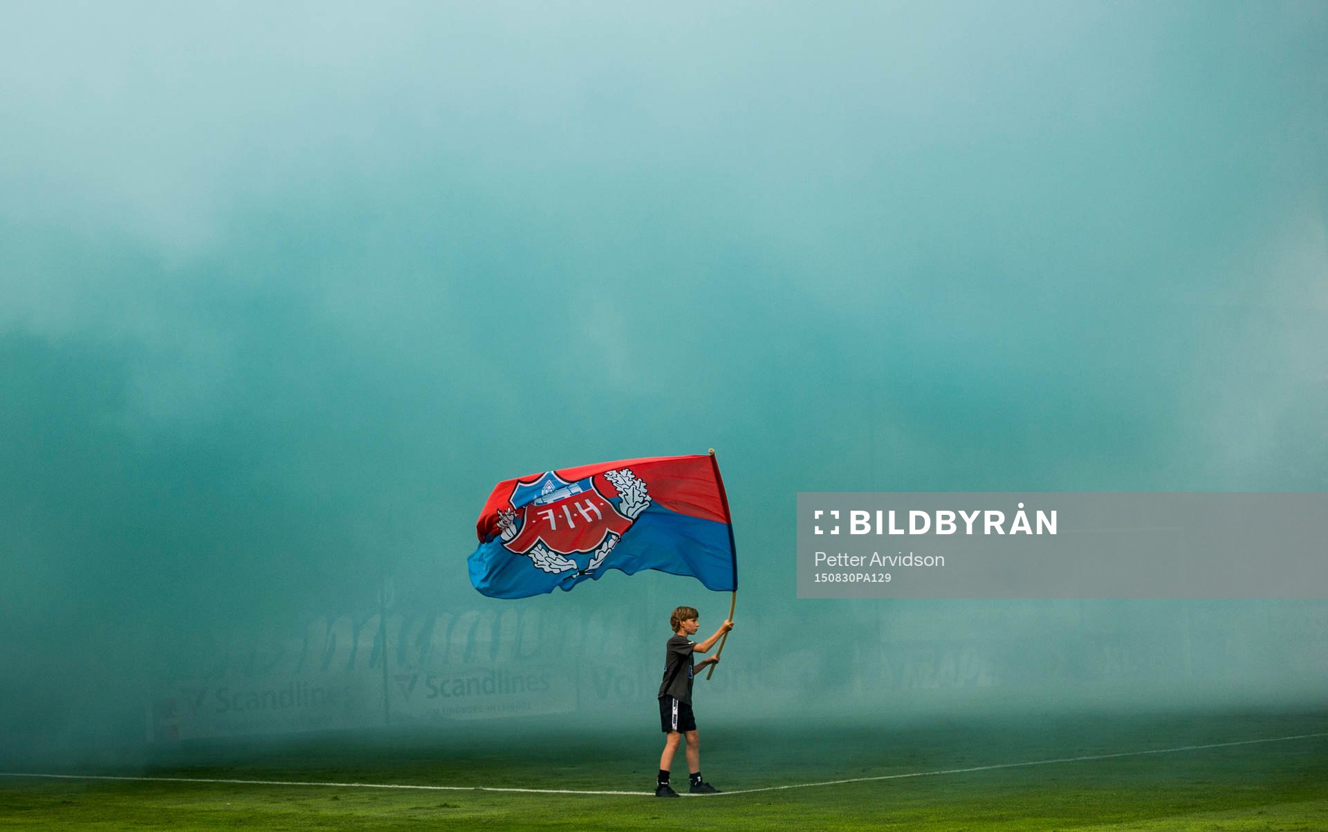 En ung pojke vevar en Helsingborg flagga i tung rök