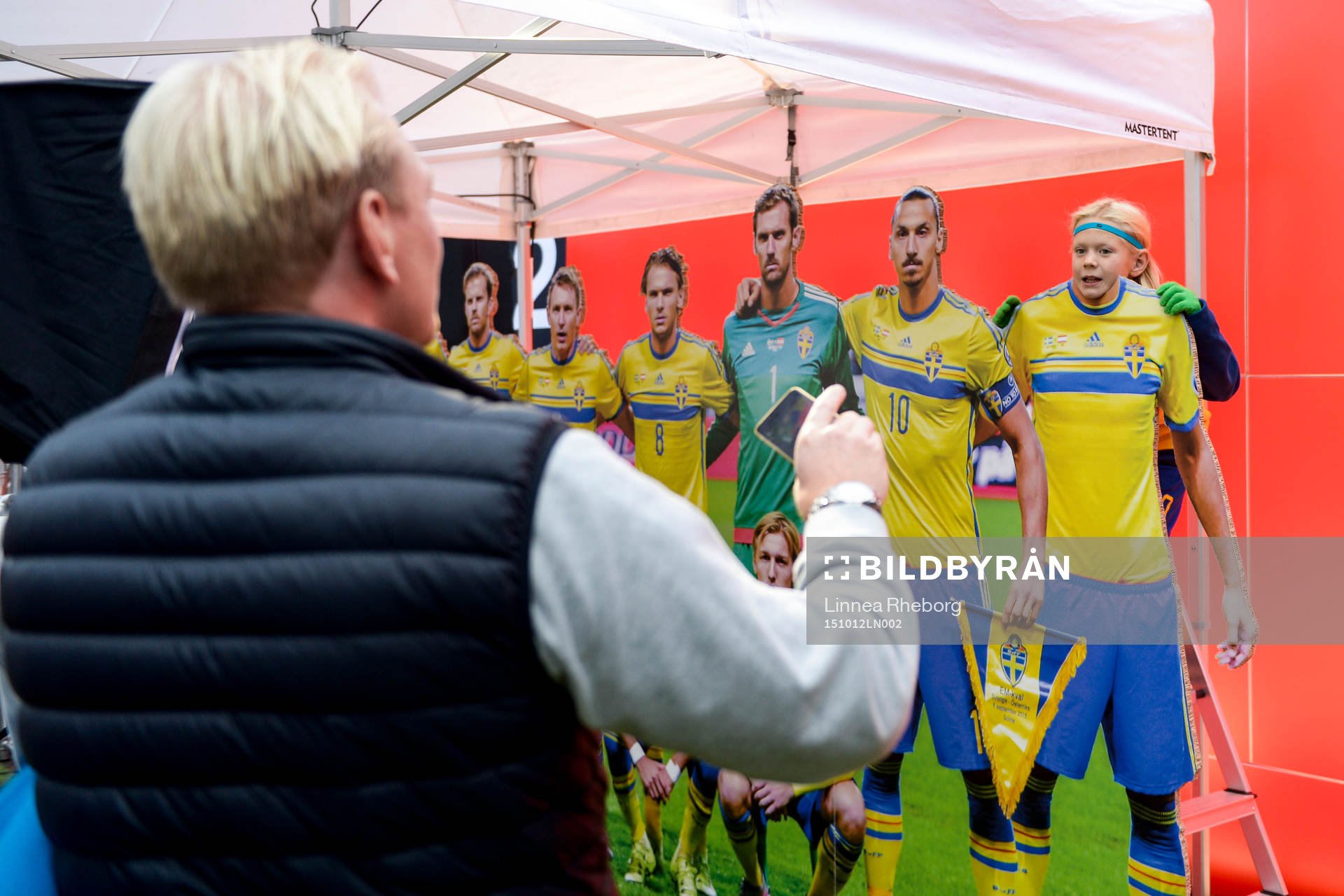 En pappa tar en bild av sin son vid en fotvägg i  Fan Zone
