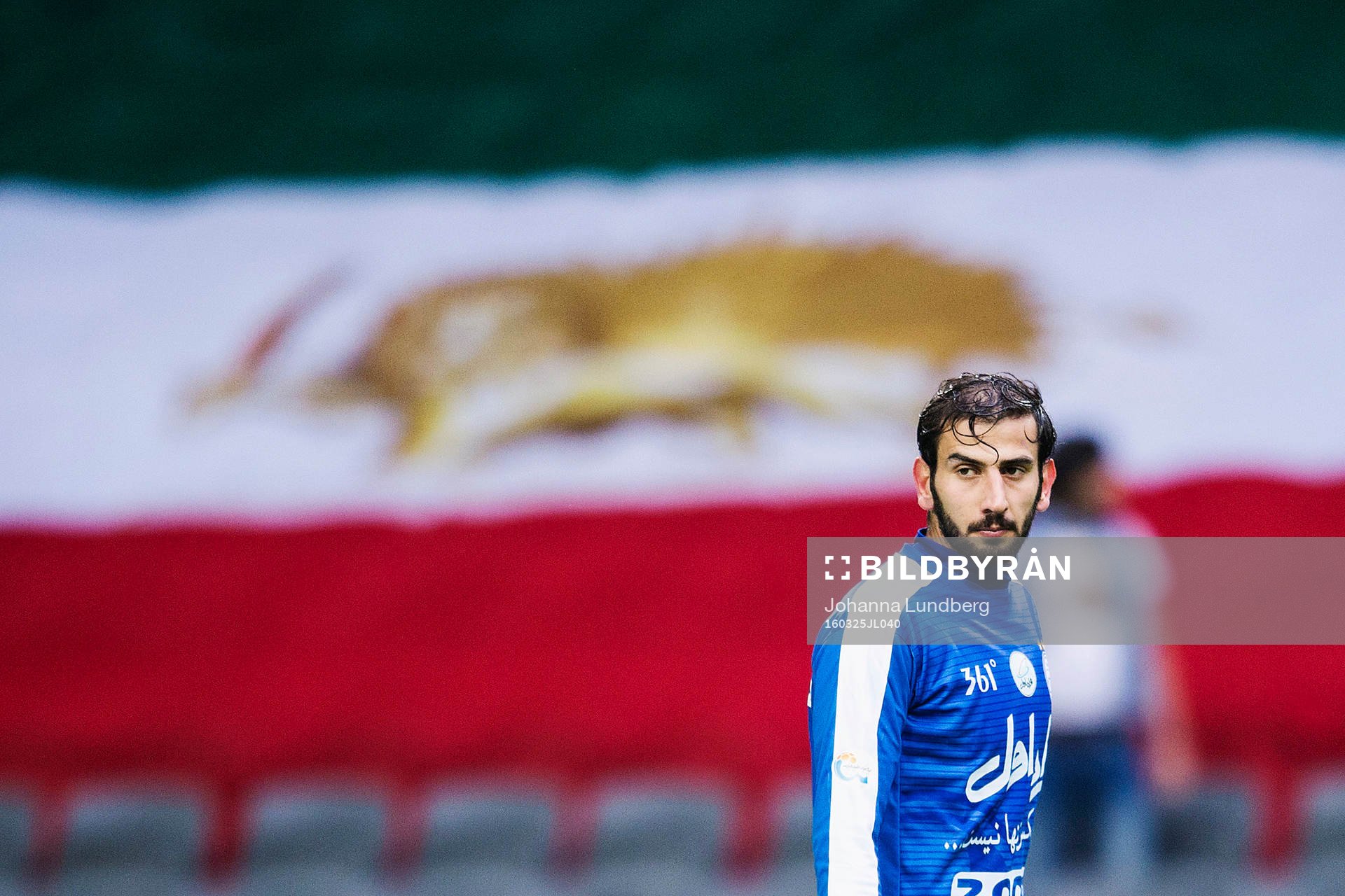 Esteghlals Amin Hajmohammadi framför en stor Iransk flagga