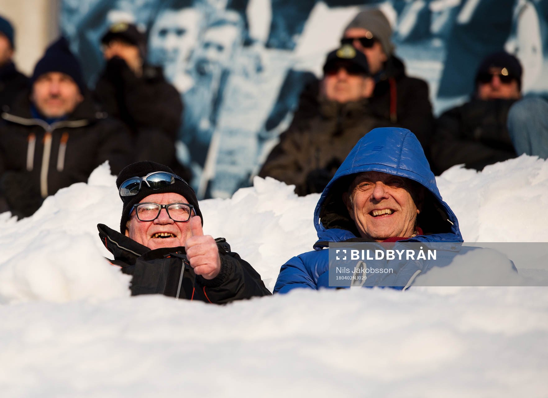 Två män sitter på läktaren mitt i snön
