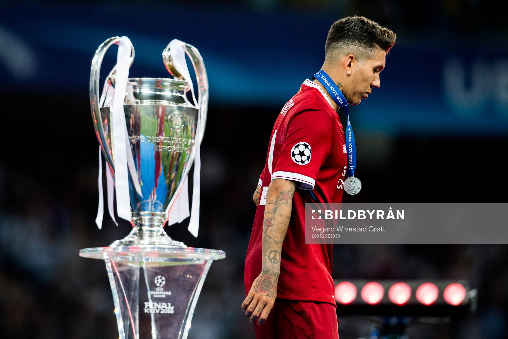 Roberto Firmino of Liverpool walks by the trophy
