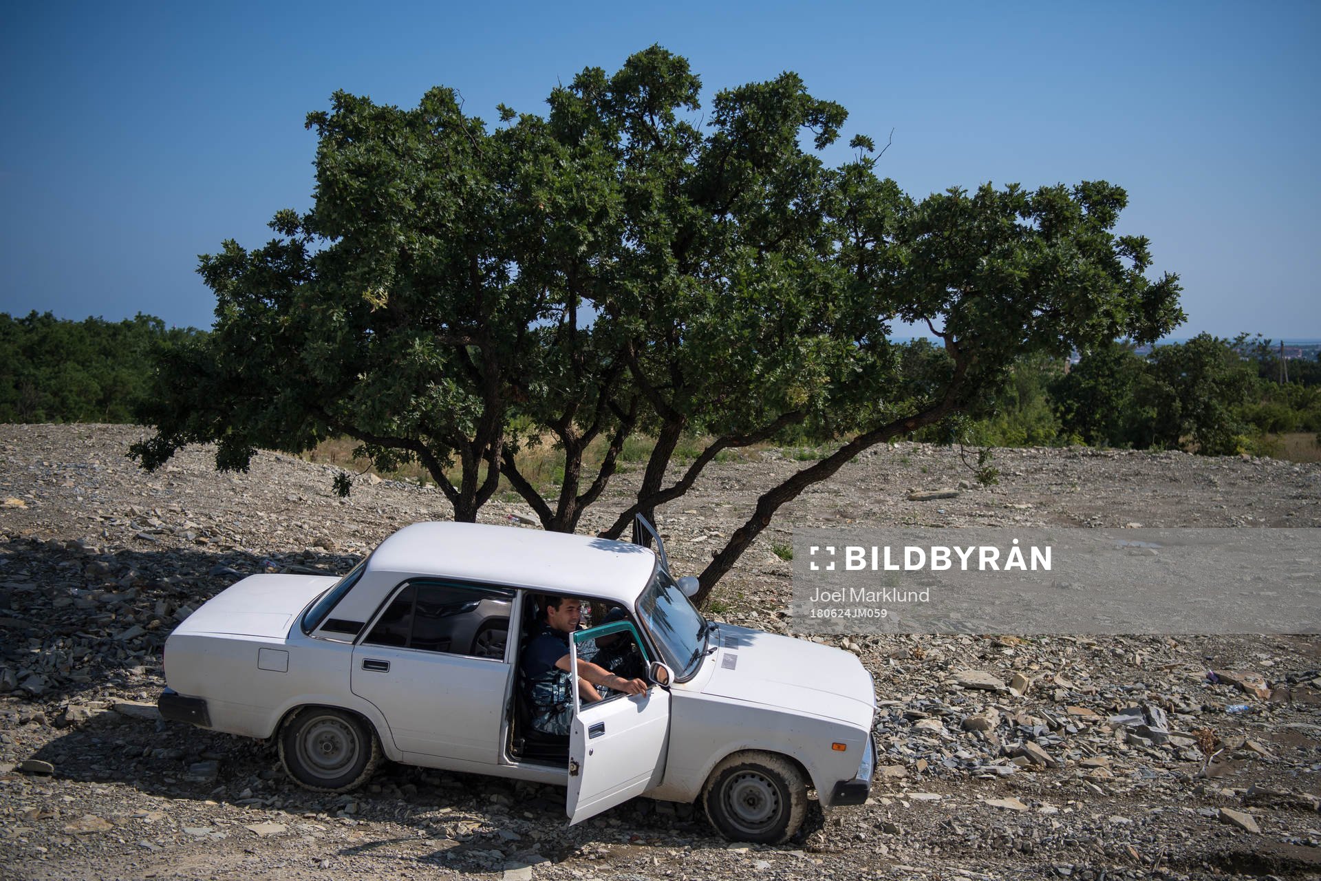 Security personel sits in a car parked by a tree