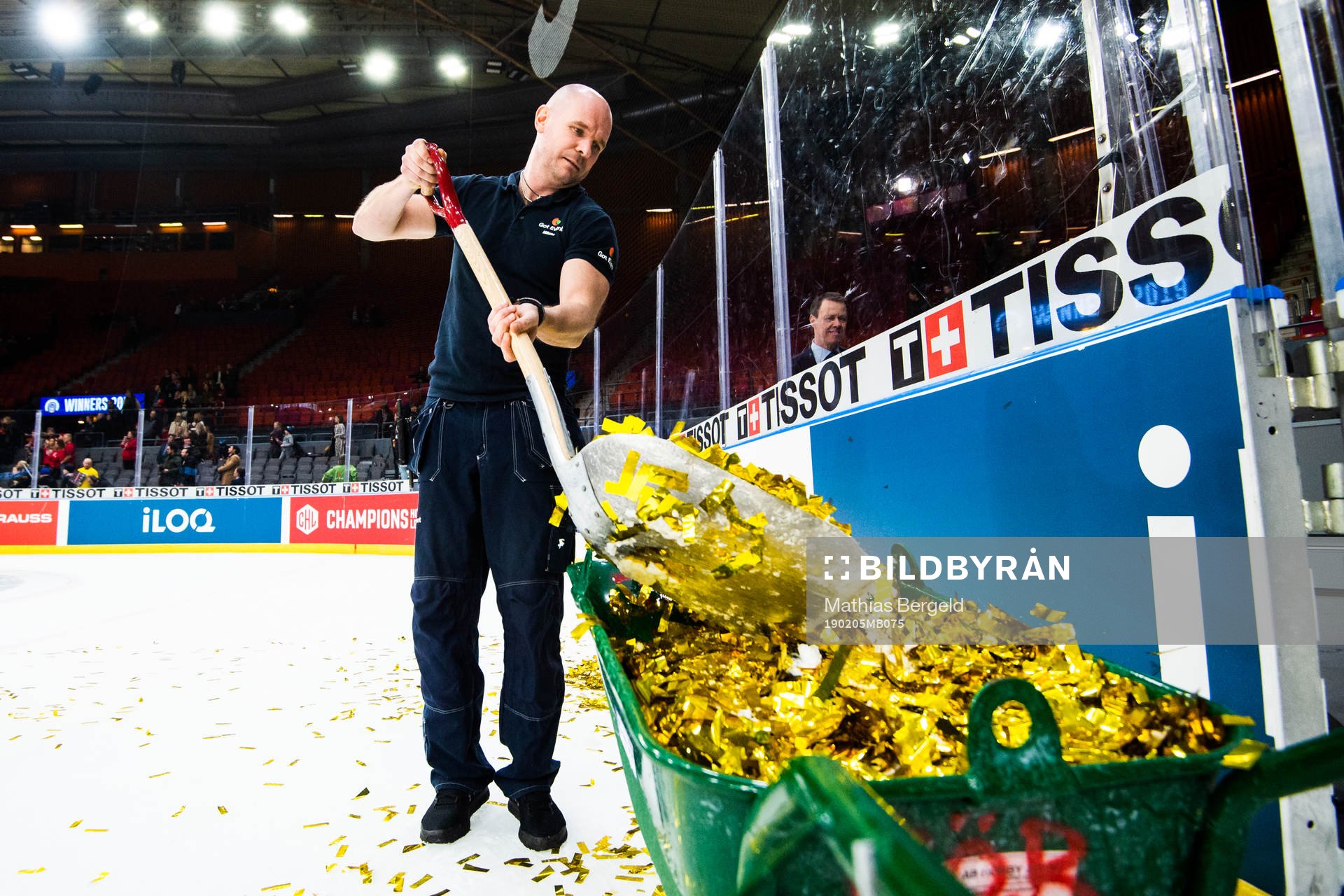 A janitor shuffles gold glitter into a wheelbarrow