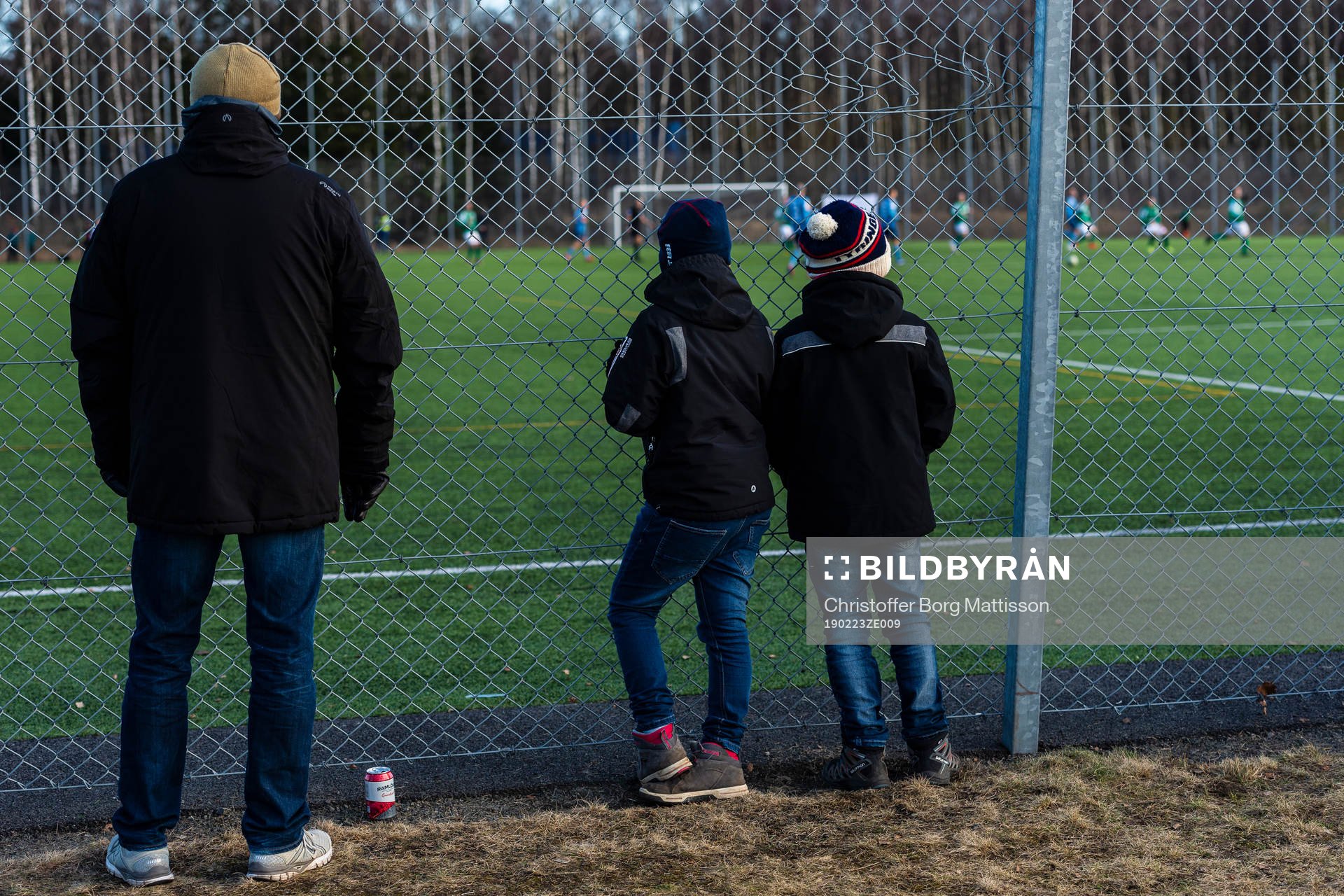 Pappa med två söner ser matchen bakom staketet