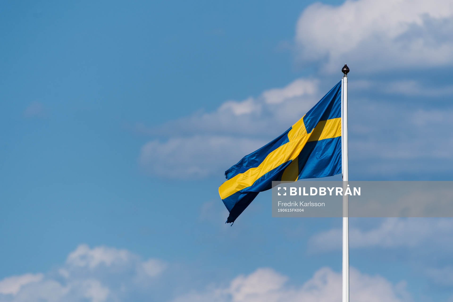 Svenska flaggan på en flaggstång med blå himmel och moln
