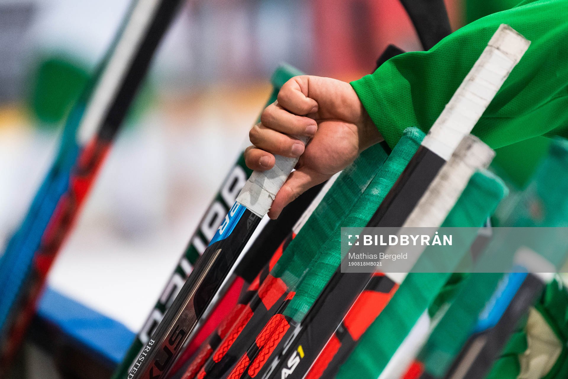 En hand tar en ishckeyklubba som står lutad mot sargen på
