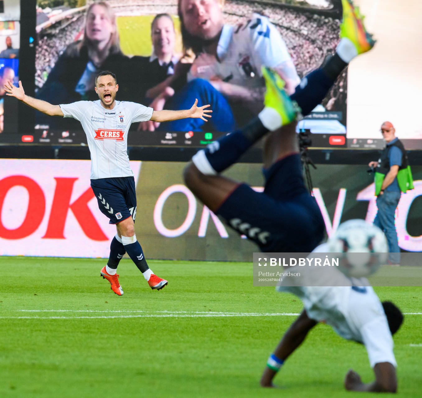 Casper Höjer Nielsen reacts as Mustapha Bundu of Aarhus falls, infront of a virtual grandstand with supporters during the Danish Superliga match between AGF Aarhus and Randers FC which are played without spectators due to the coronavirus covid-19, on May 28, 2020 in Aarhus.