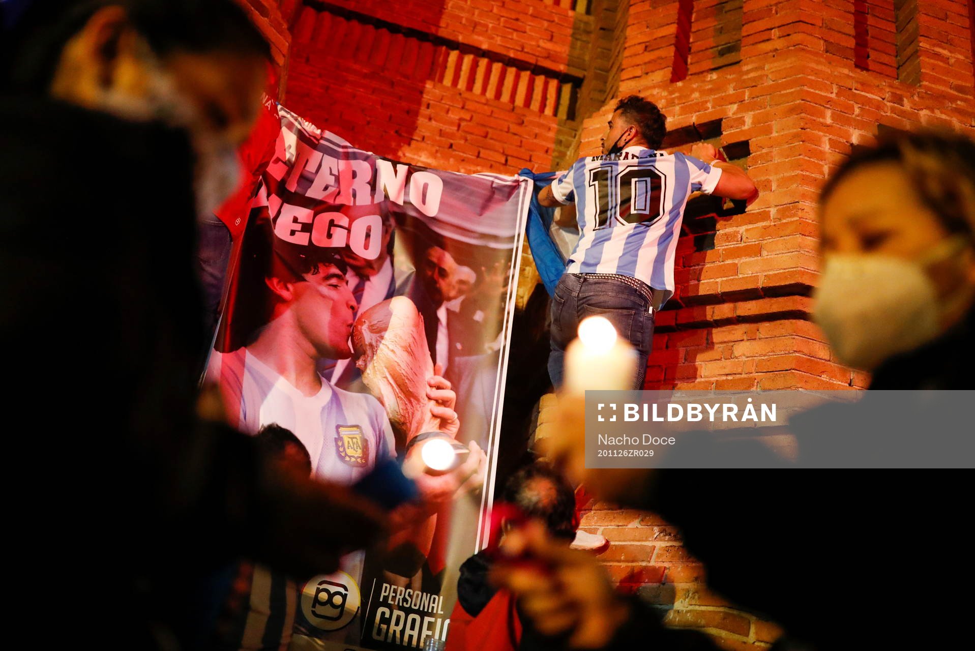 Soccer fans light candles next to a poster with the image
