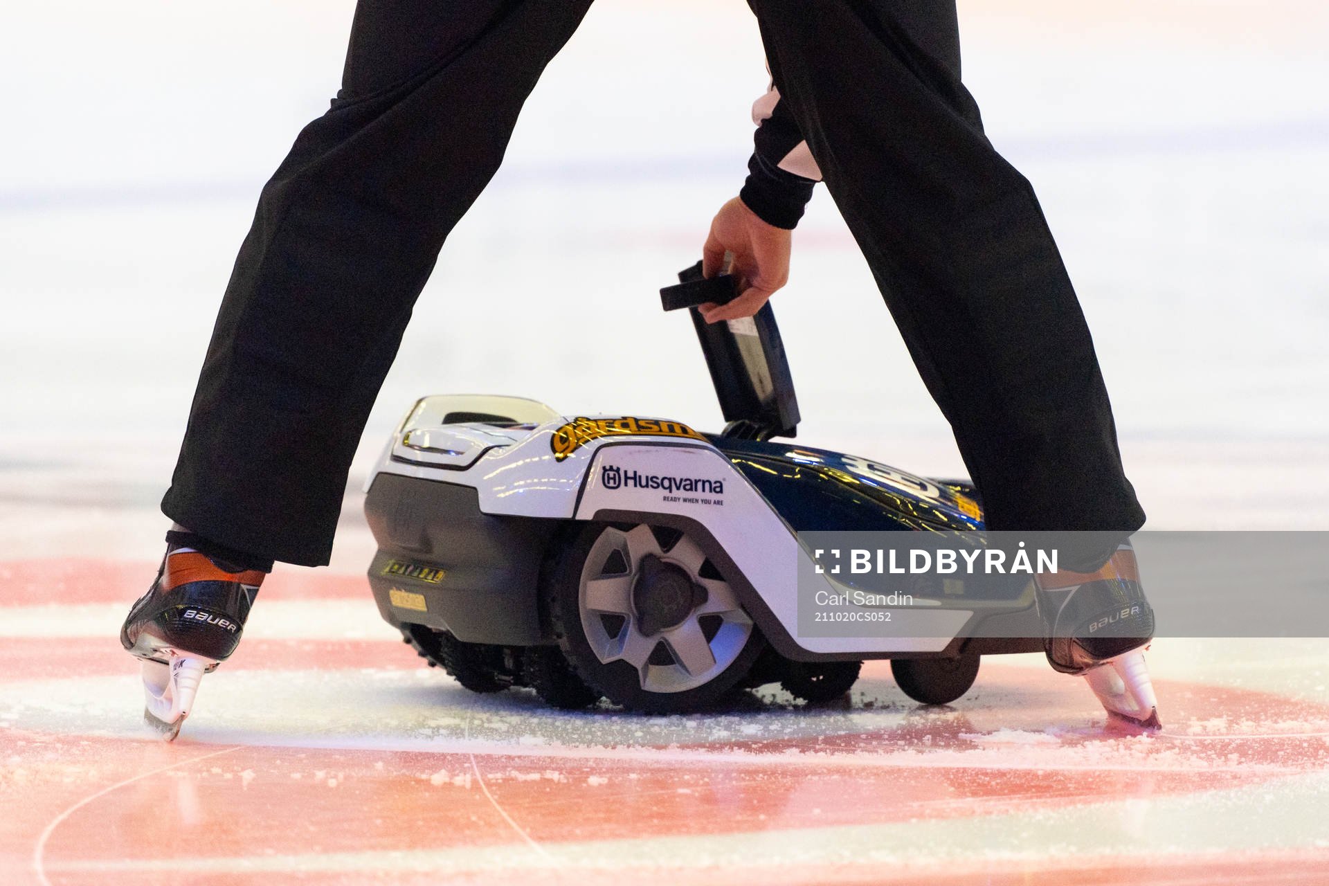 Domaren plockar upp matchpucken ur en robotgräsklippare