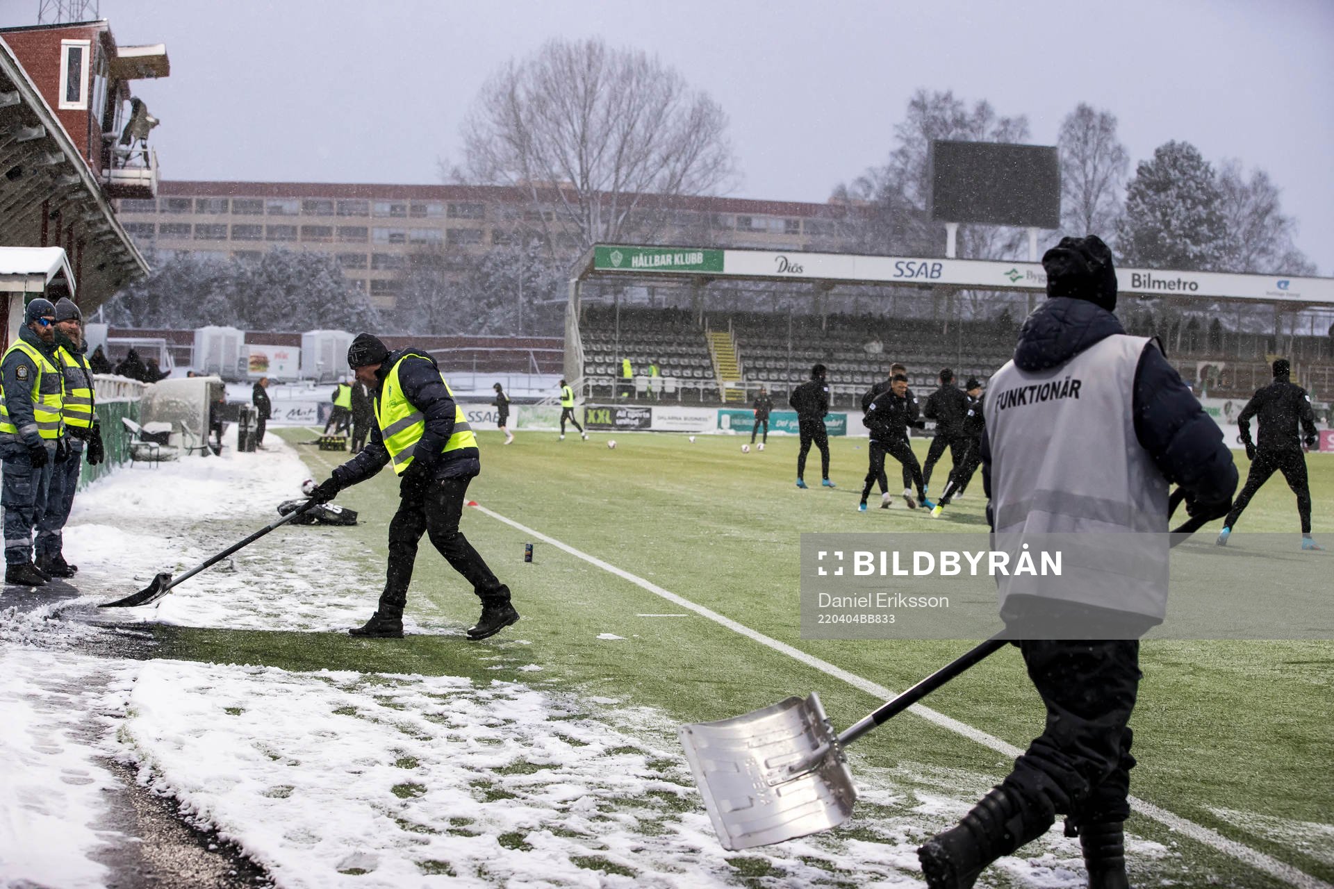 Funktionärer skottar snö innan fotbollsmatchen i