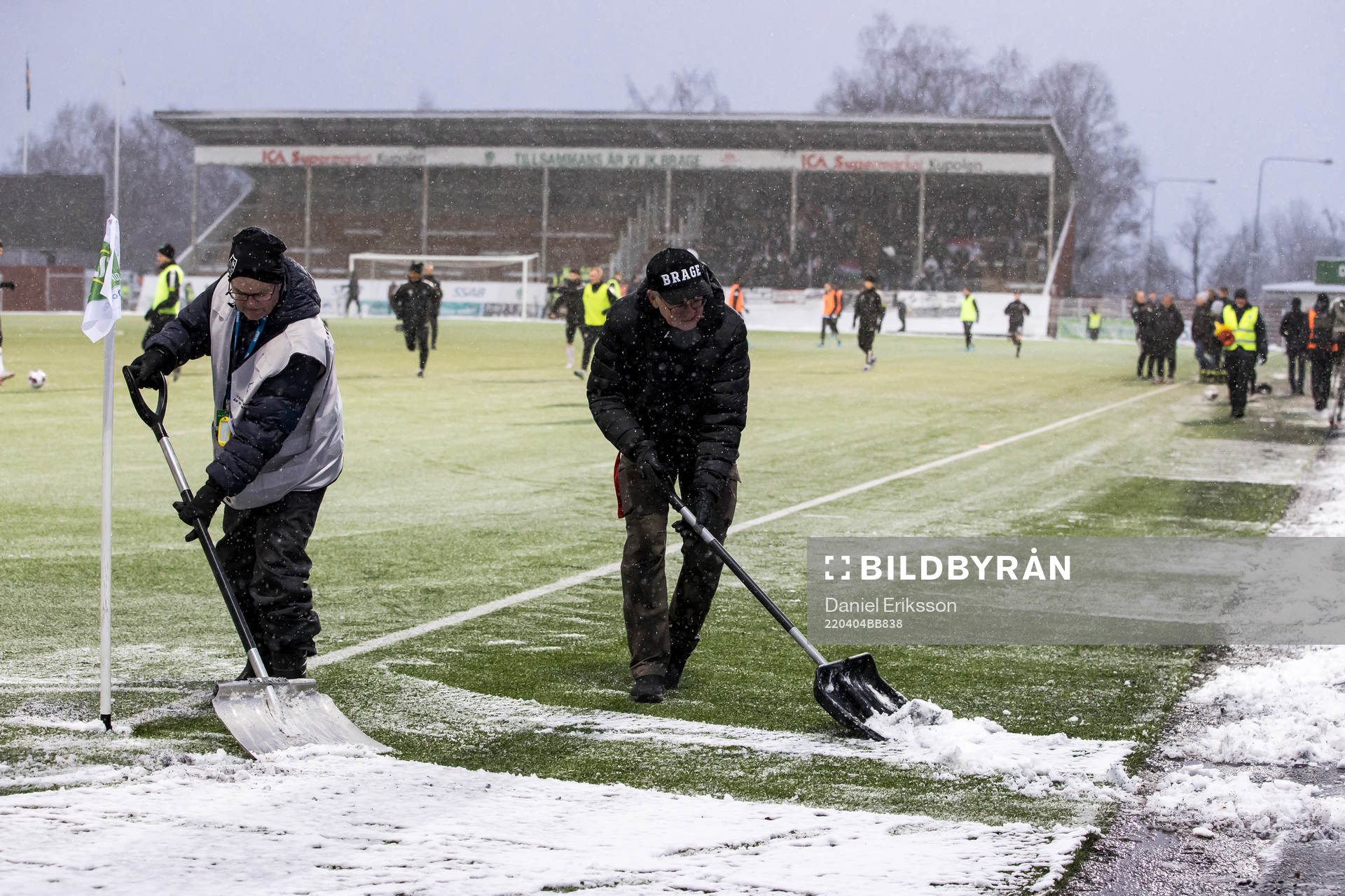 Funktionärer skottar snö innan fotbollsmatchen i