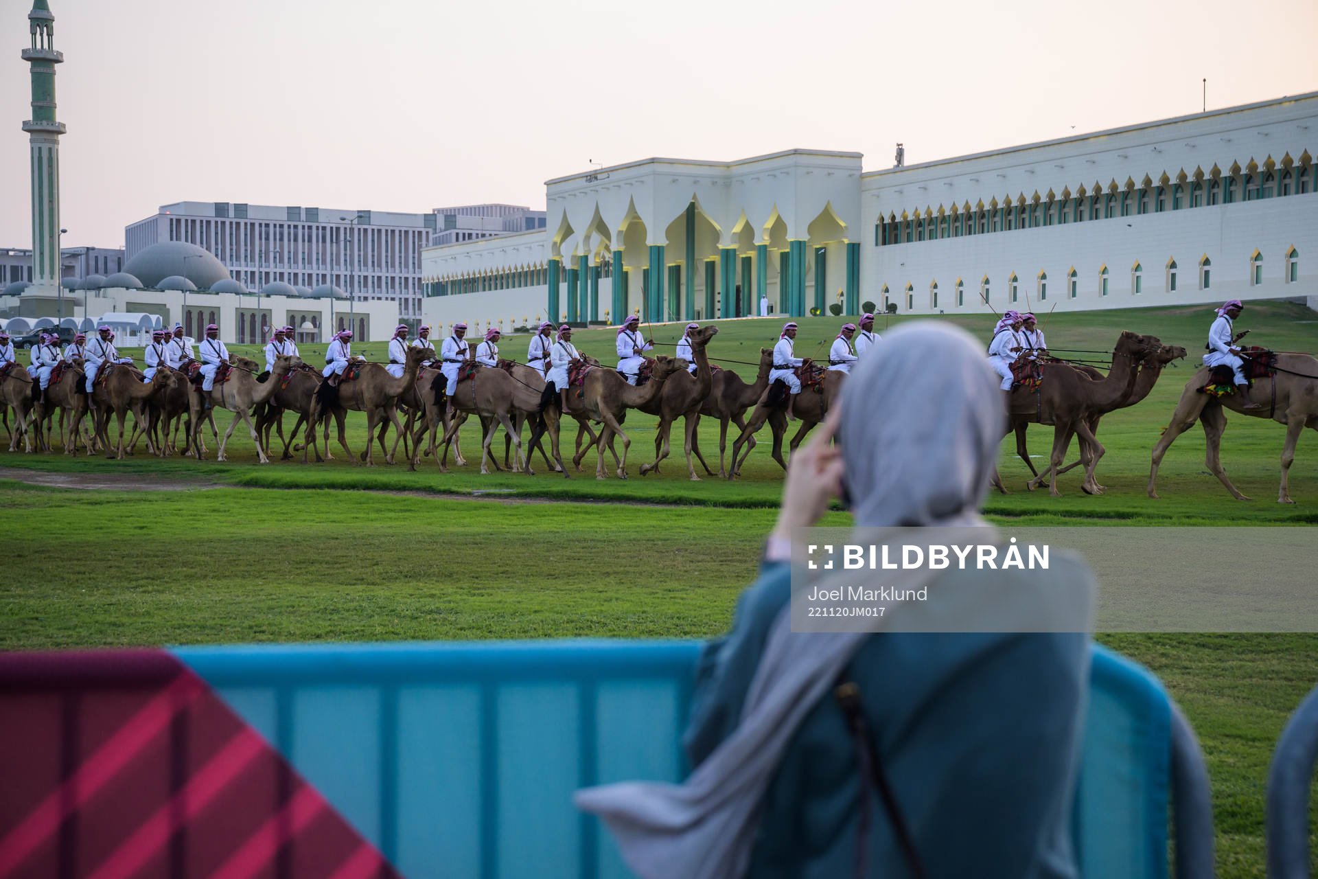 A woman takes photos of camels riding in front of