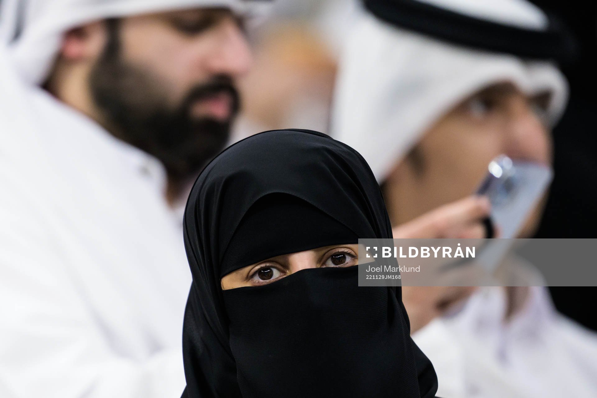 A woman wearing a niqab in front of two men in Qatari