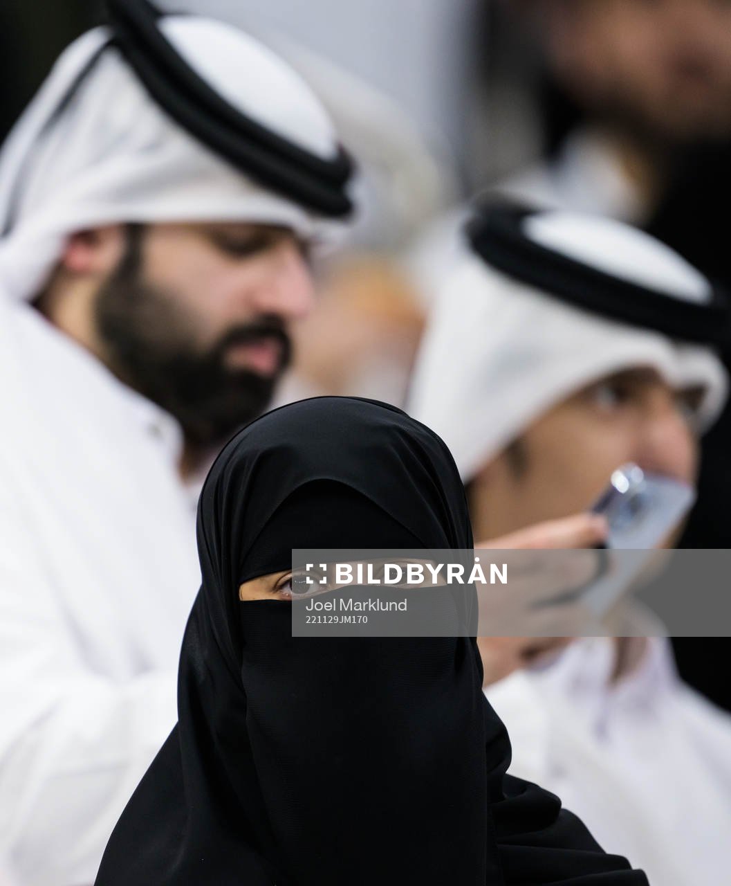 A woman wearing a niqab in front of two men in Qatari