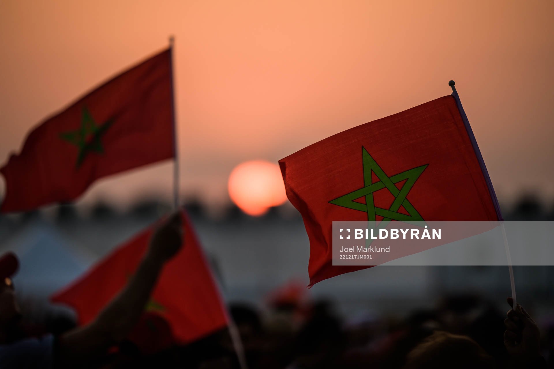 People wave Moroccan flags at sunset