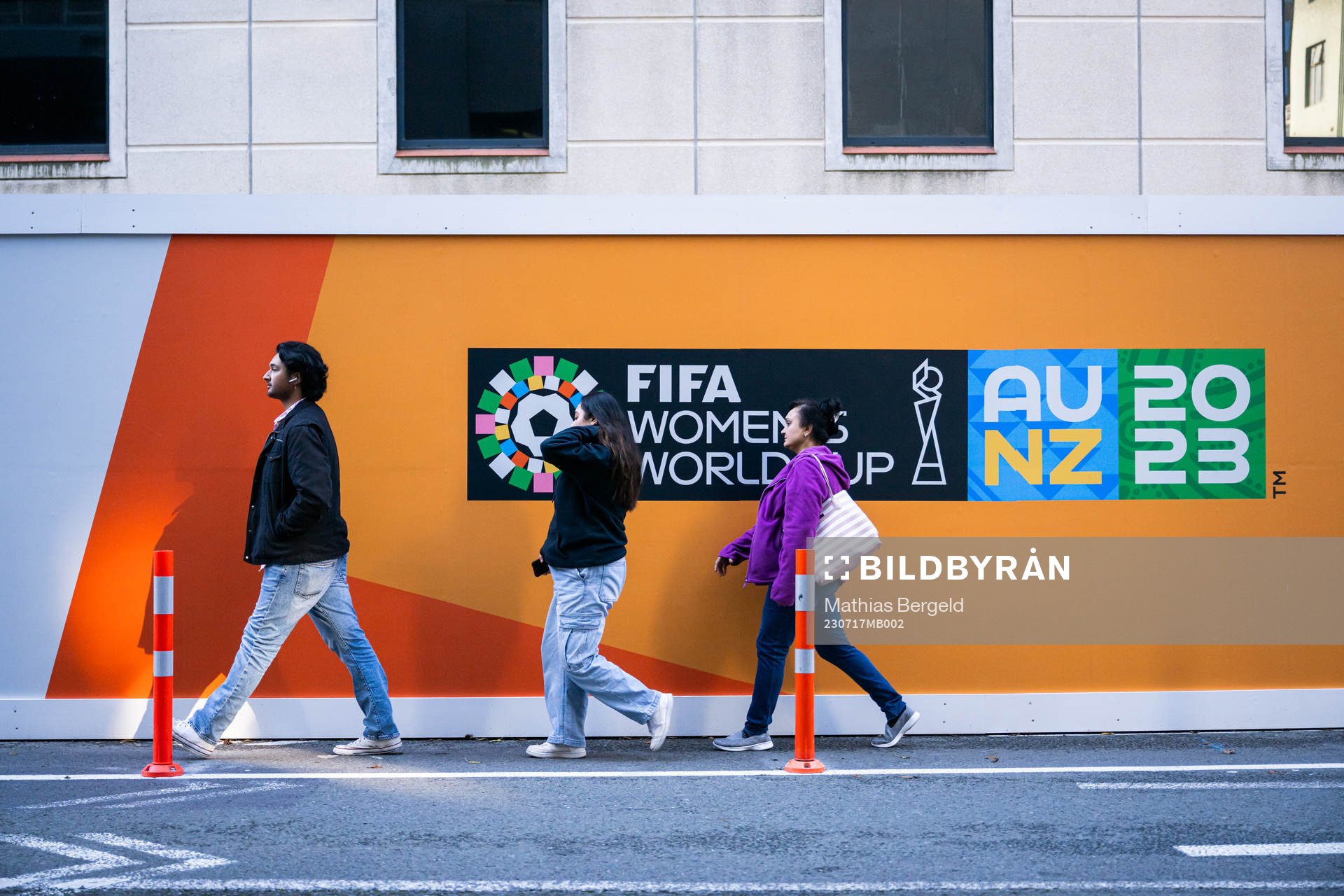 Three persons walk past a board with the logo for FIFA