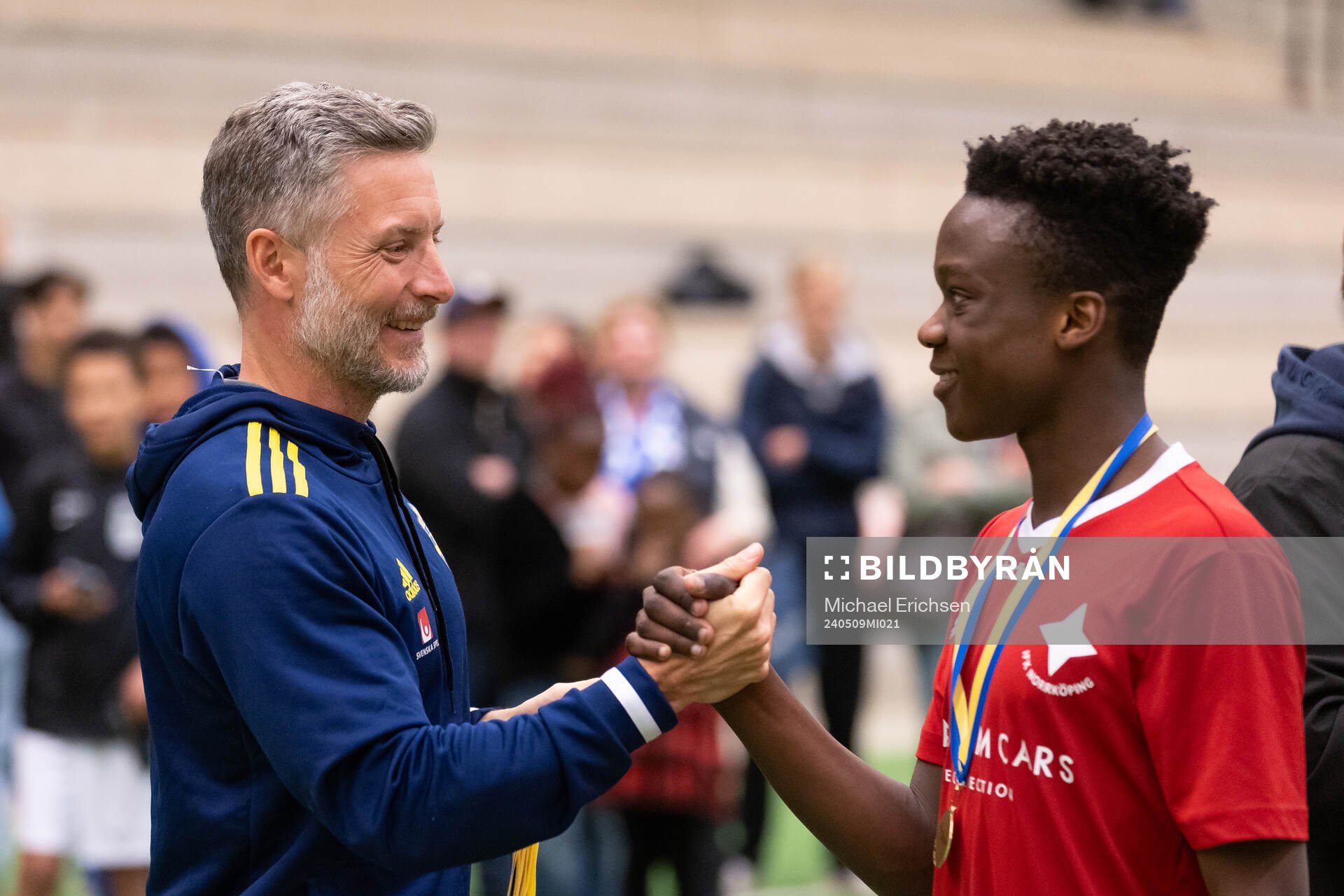 Det svenska P16-landslagets förbundskapten Axel Kjäll delar ute en guldmedalj till IFK Norrköpings Emmanuel Alase efter finalen i ligacupen för P17 mellan IFK Göteborg och IFL Norrköping den 9 maj 2024 i Prioritet Serneke Arena.