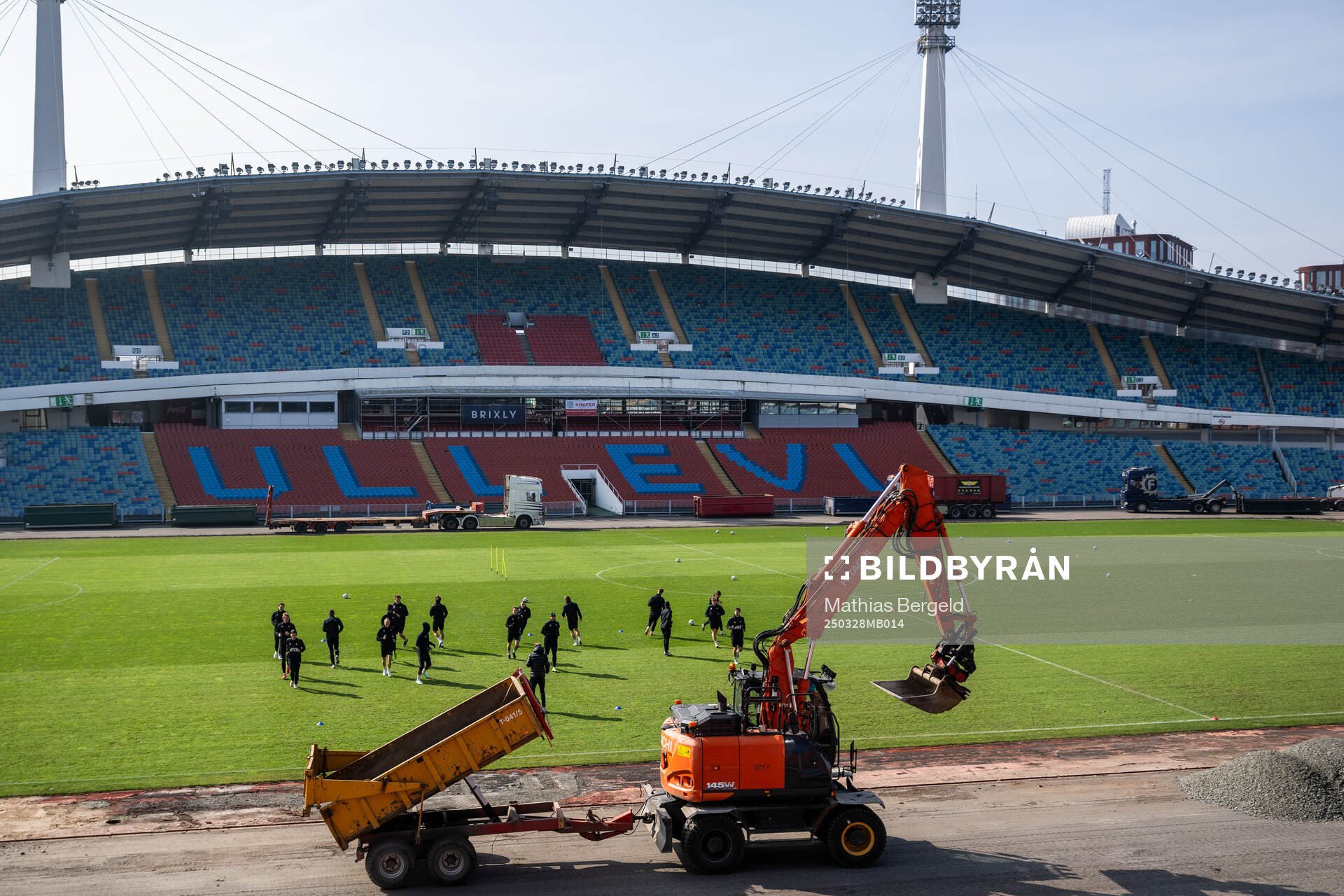 En grävmaskin kör förbi medan spelarna värmer upp