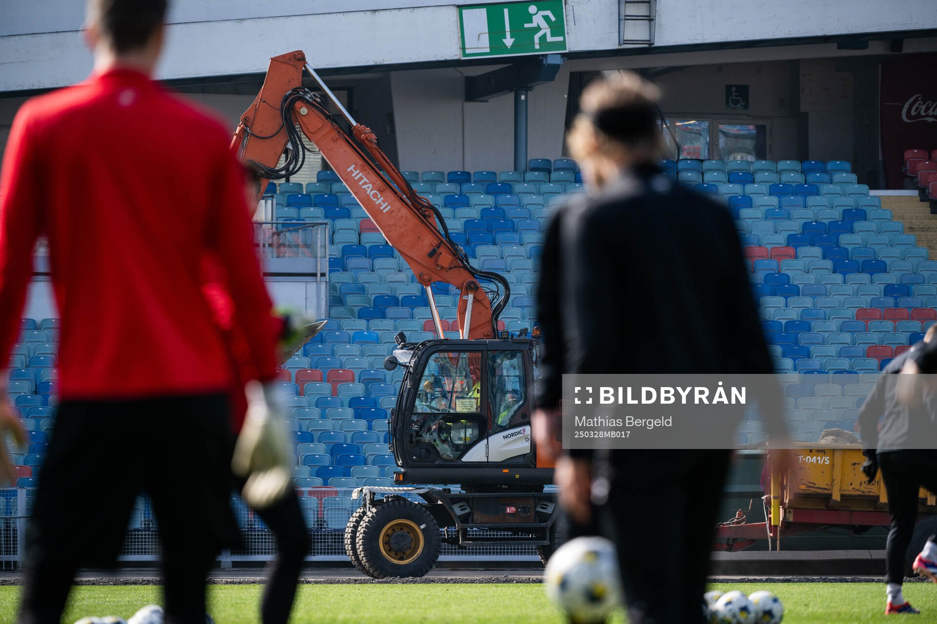 En grävmaskin kör förbi medan spelarna värmer upp