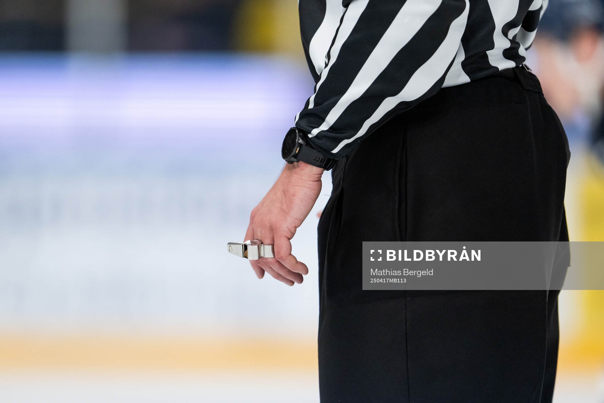 A hand of a referee holds a whistle