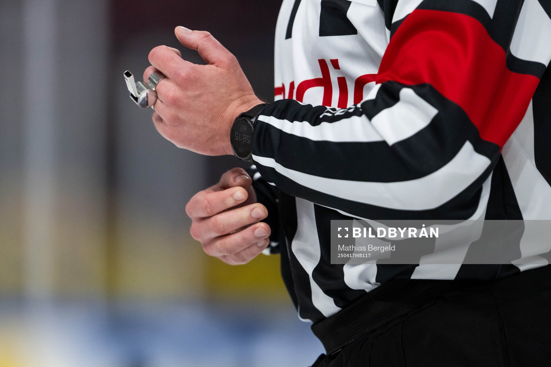 A hand of a referee holds a whistle