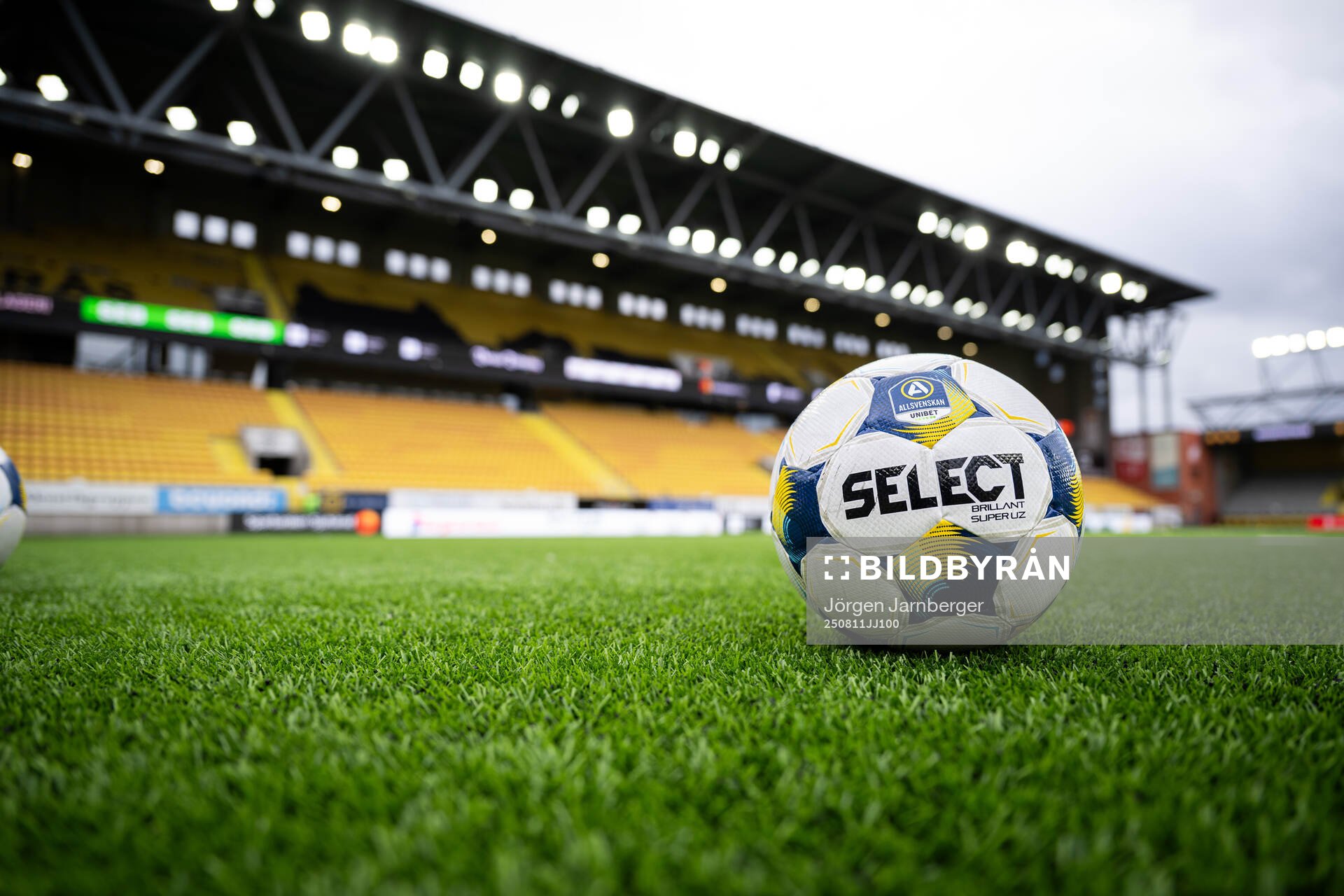 Select fotboll på konstgräset med läktare i bakgrunden