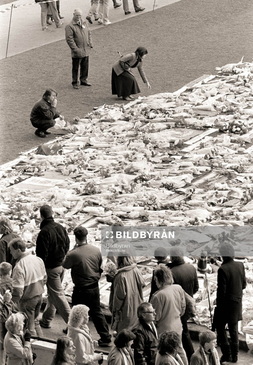 People look at a sea of flowers and scarves at Anfield to