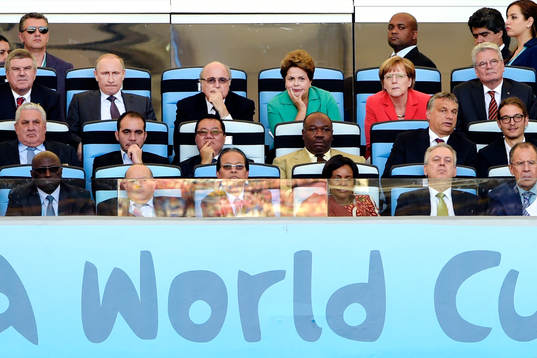 På läktaren sitter blandannat Rysslands president Vladimir Putin, FIFAs president Sepp Blatter, Brasiliens president Dilma Rousseff och Tysklands förbundskansler Angela Merkel