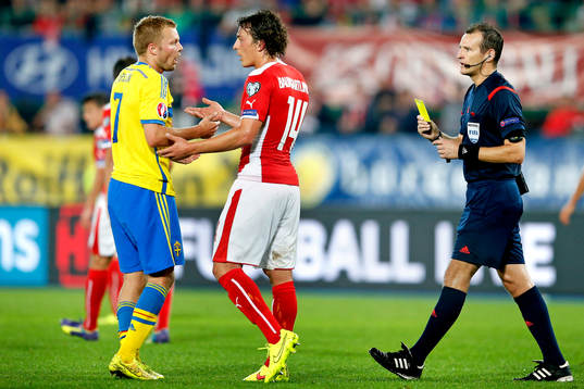 Sveriges Sebastian Larsson (tv) pratar med Österrikes Julian Baumgartlinger (mitten) efter att ha blivit varnad av domare Pavel Kralovec (th)
