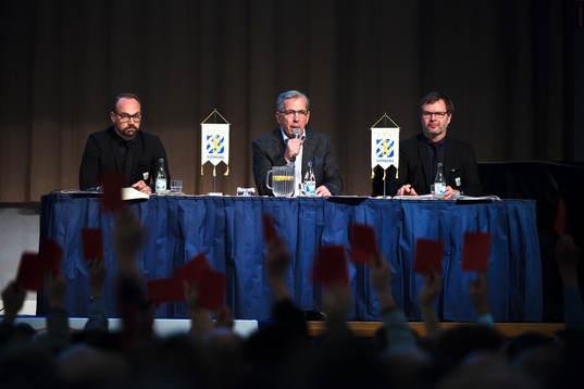 Styrelseledamot Olof Myhrman, Jan Hallberg och ordförande Karl Jartun ser på när medlemmar röstar med röda lappar