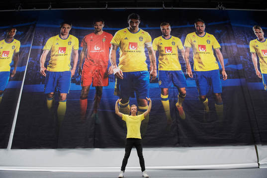 Bildbyråns fotograf Joel Marklund poserar framför en bild - som är tagen av honom - med porträtt på Kim Källström, Andreas Isaksson, Zlatan Ibrahimovic, Sebastian Larsson och Andreas Granqvist i presscentret