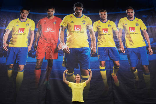 Bildbyråns fotograf Joel Marklund poserar framför en bild - som är tagen av honom - med porträtt på Kim Källström, Andreas Isaksson, Zlatan Ibrahimovic, Sebastian Larsson och Andreas Granqvist i presscentret