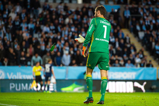 Djurgårdens målvakt Andreas Isaksson rensar bort en ölflaska som blivit inkastad på planen