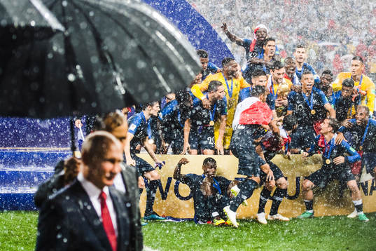 The president of Russia, Vladimir Putin walks in front of photographers while players of France celebrate with the trophy