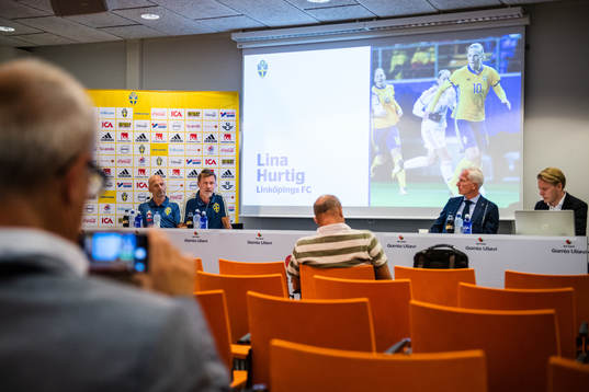 En bild på Lina Hurtig, som tagits ut i landslagstruppen, syns  bakom assisterande förbundskapten Magnus Wikman, förbundskapten Peter Gerhardsson, Svenska fotbollsförbundets generalsekreterare Håkan Sjöstrand och pressansvarig Fredrik Madestam