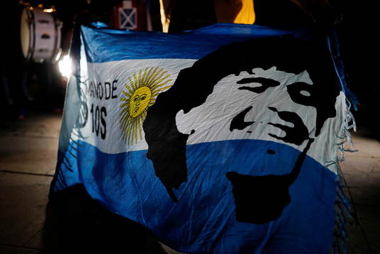  A soccer fan holds an Argentine flag with the face of late Argentine soccer legend Diego Armando Maradona painted on it during a tribute to him the day after his death, in Barcelona, Spain, November 26, 2020.  REUTERS/Nacho Doce 