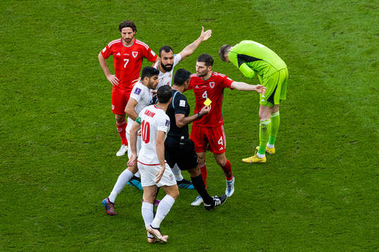 Karim Ansarifard of Iran with Joe Allen and Ben Davies of Wales as they react towards the referee as goalkeeper Wayne Hennessey receives a yellow card (that is changed to a red after VAR review) the referee