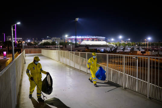 Stadium 974 is seen in the background as migrant workers clean a pathway on a bridge to reach the metro station Ras Bu Abboud