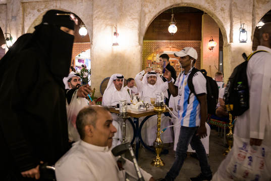 Qatari men see an Argentinian fan and Qatari woman in niqab walk by