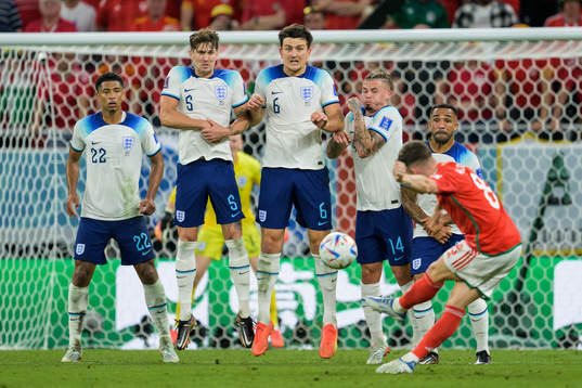 Jude Bellingham, John Stones, Harry Maguire, and Kalvin Phillips of England form a wall as Harry Wilson of Wales takes a freekick