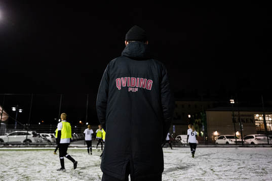En ledare med klubbnamnet på jackan tittar på spelare från akademin
